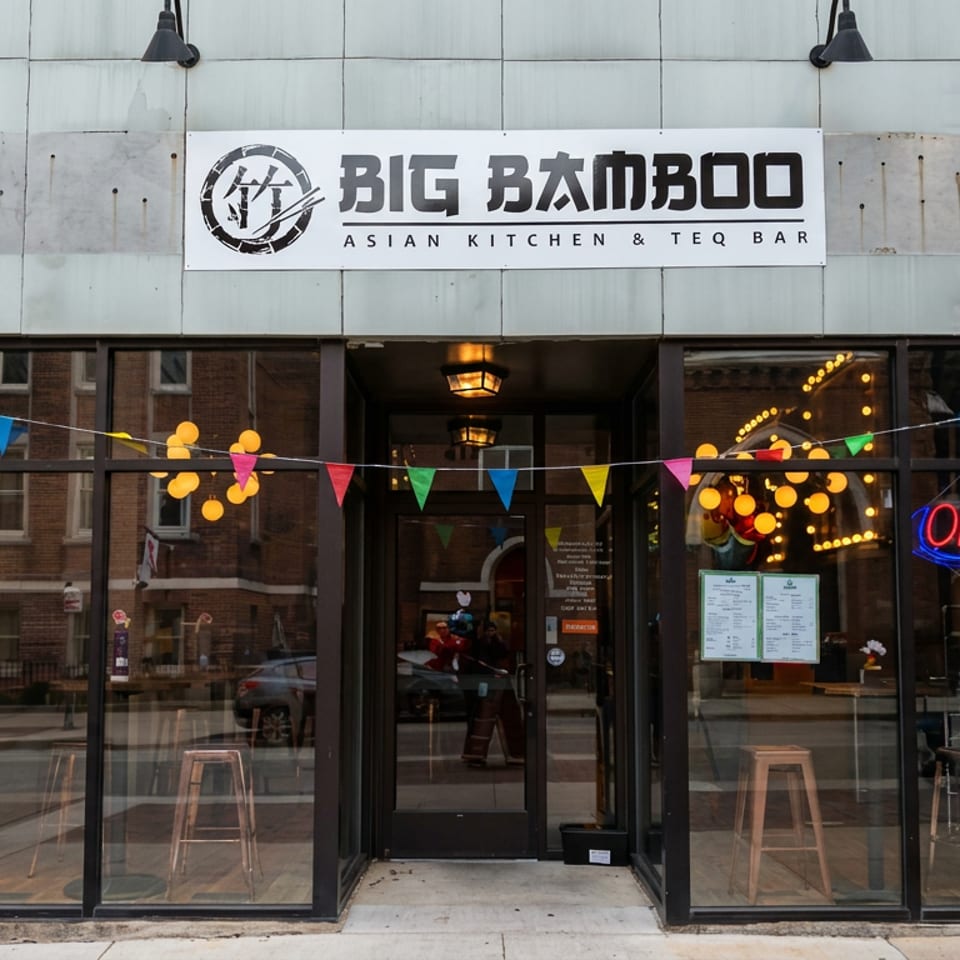 Big Bamboo Asian Kitchen & Teq Bar storefront with colorful bunting, illuminated open sign, and visible bar stools.