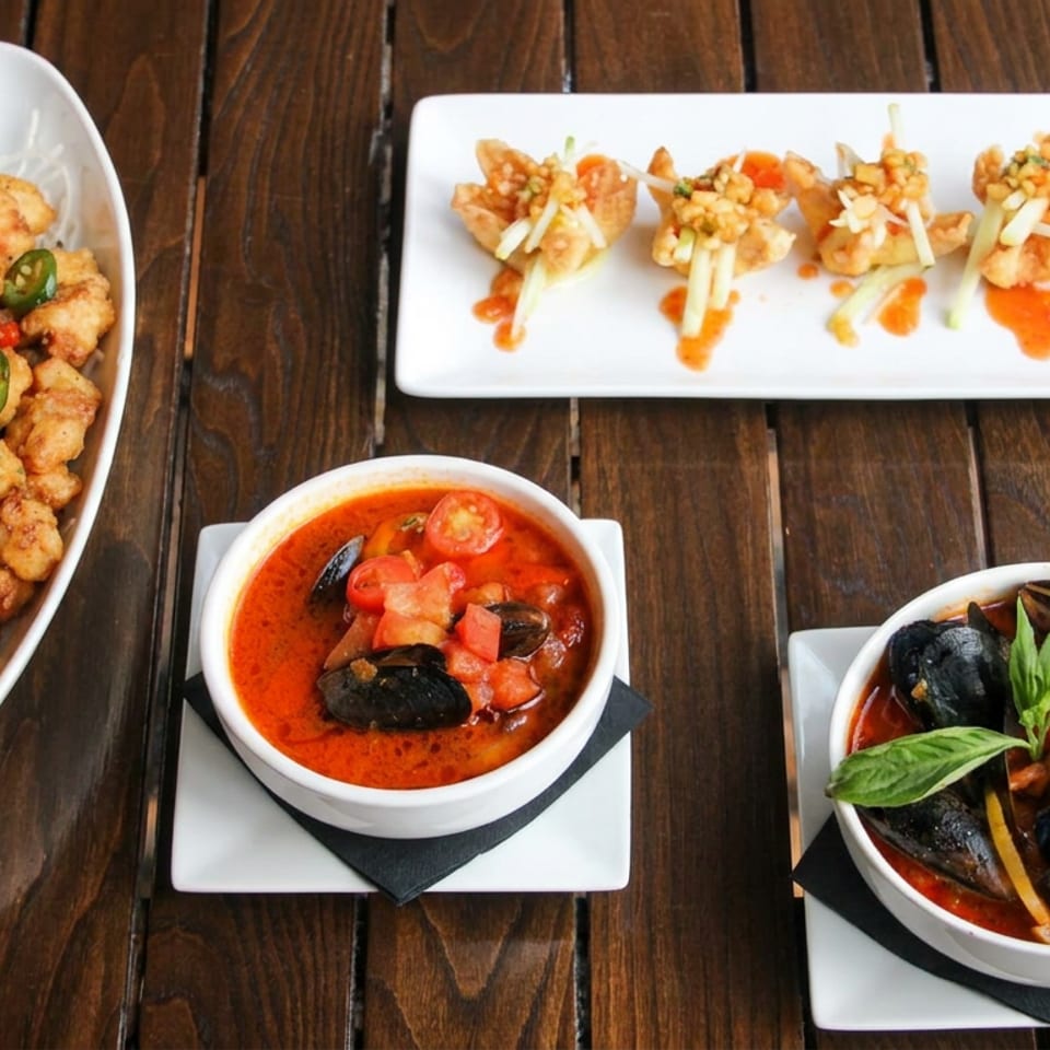 Assorted seafood dishes on a wooden table, including fried bites, skewered shrimp, mussels in tomato sauce, and basil garnish.