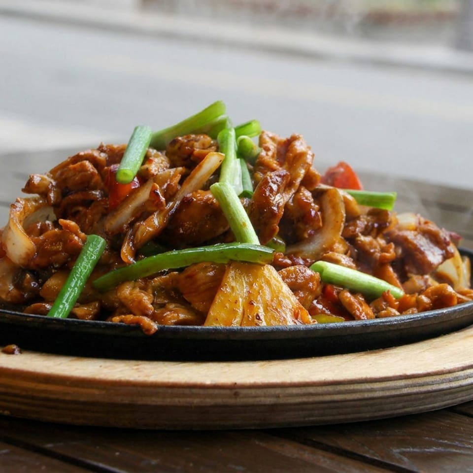 Sizzling stir-fried meat and vegetables with green onions served on a black platter atop a wooden serving board.