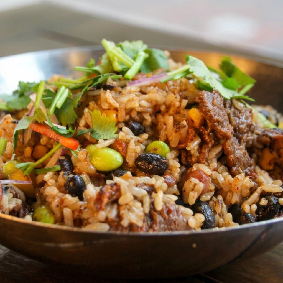 Bowl of seasoned rice with black beans, vegetables, beef, and fresh cilantro garnish on a wooden table.
