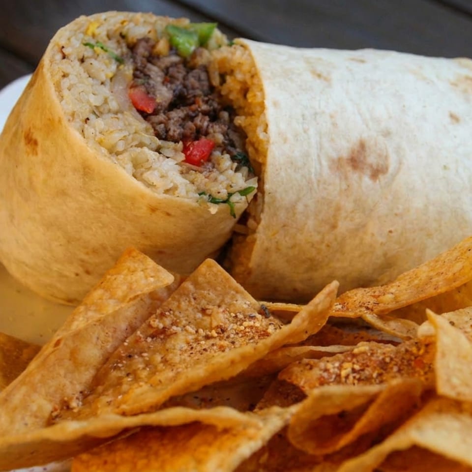 Sliced burrito filled with rice, seasoned ground meat, peppers, and herbs served with spiced tortilla chips on a white plate.
